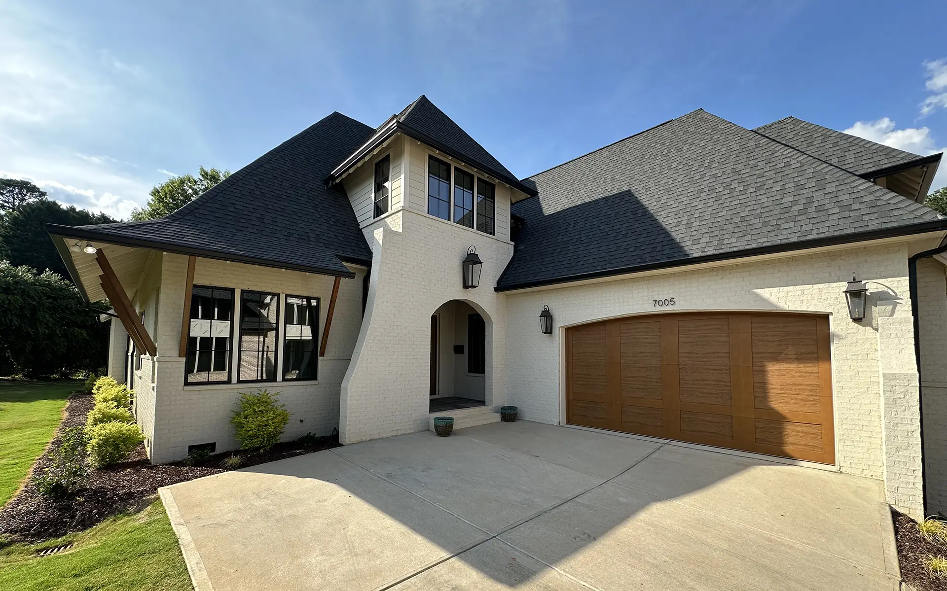 A contemporary white brick house with a dark shingle roof and wooden garage door under a clear blue sky.
