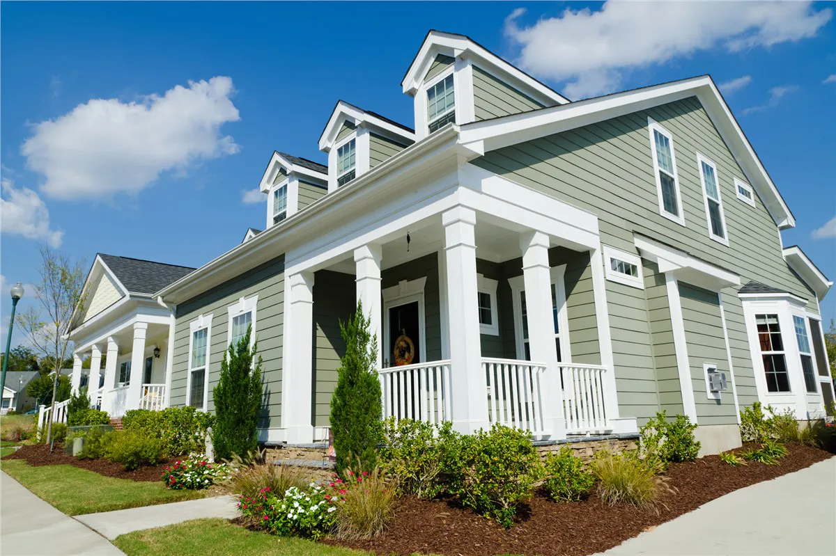 A gray two-story house with white trim and a front porch under a blue sky.