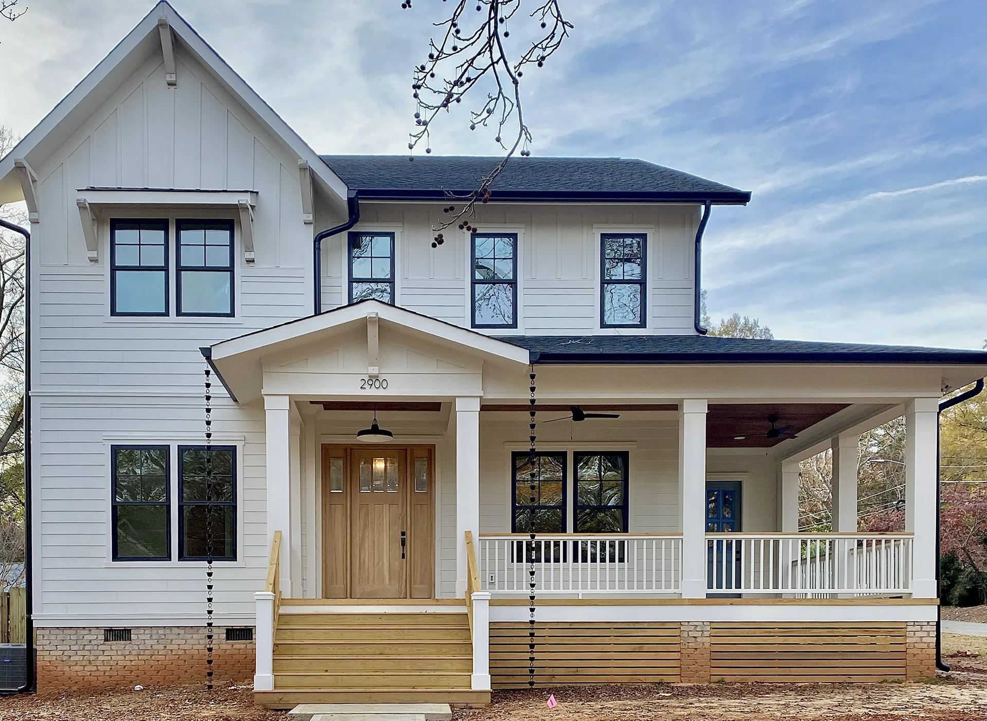 A two-story white house with a covered front porch, wooden door, and black-trimmed windows under a partly cloudy sky.