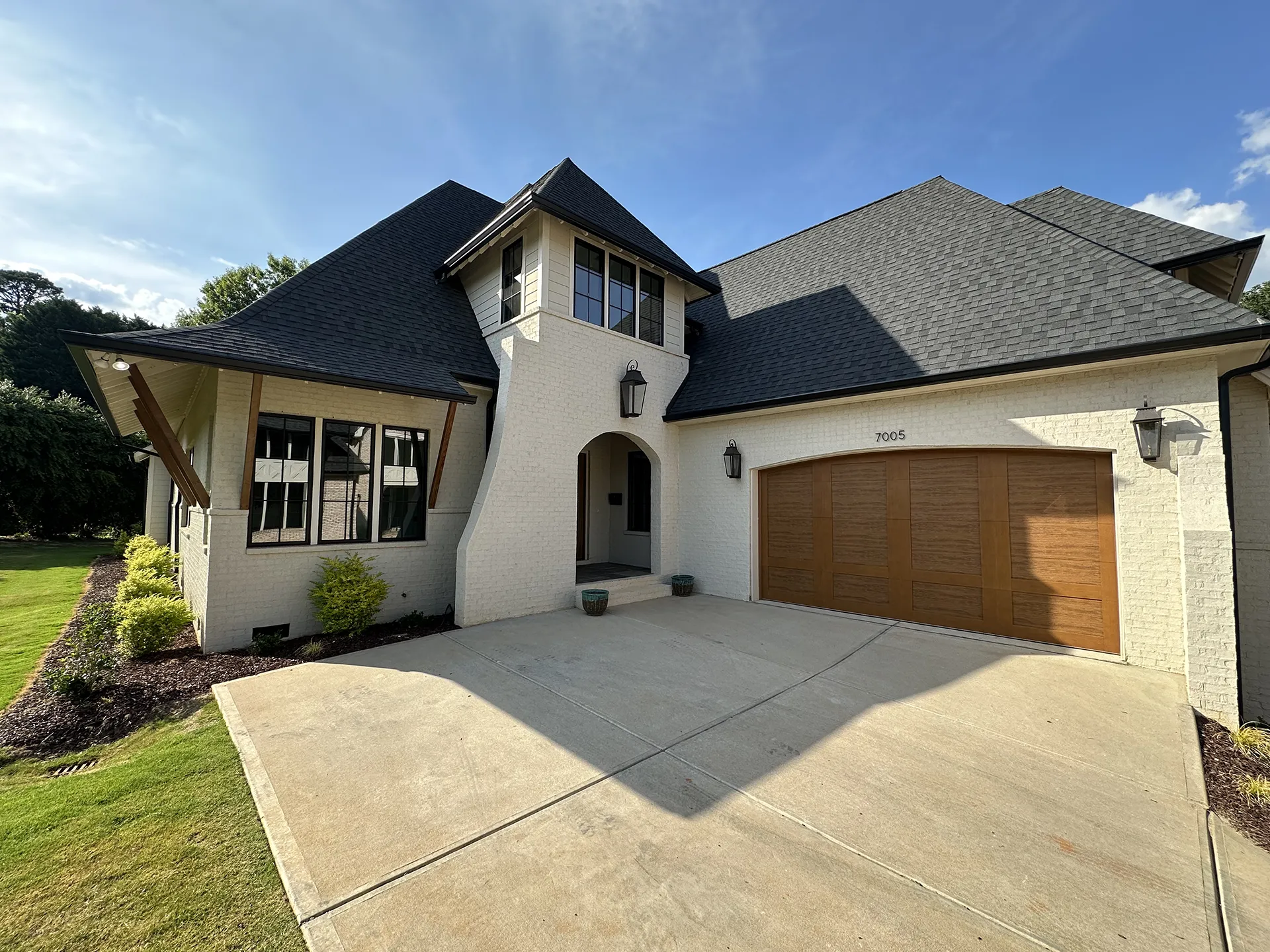 A contemporary white brick house with a dark shingle roof and wooden garage door under a clear blue sky.